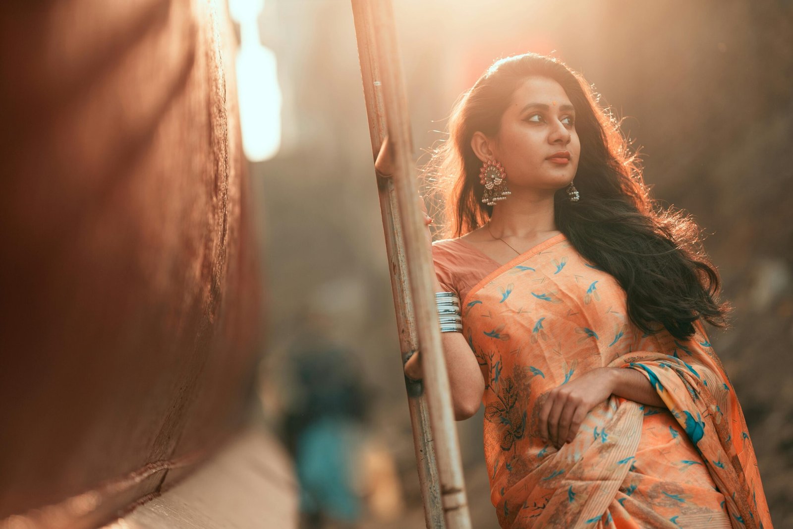 An adult woman in a traditional saree poses outdoors, illuminated by soft sunlight.