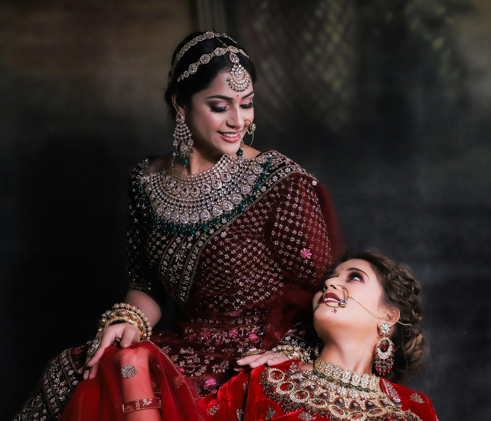 Two South Asian women in exquisite traditional outfits adorned with intricate jewelry, showcasing cultural elegance.